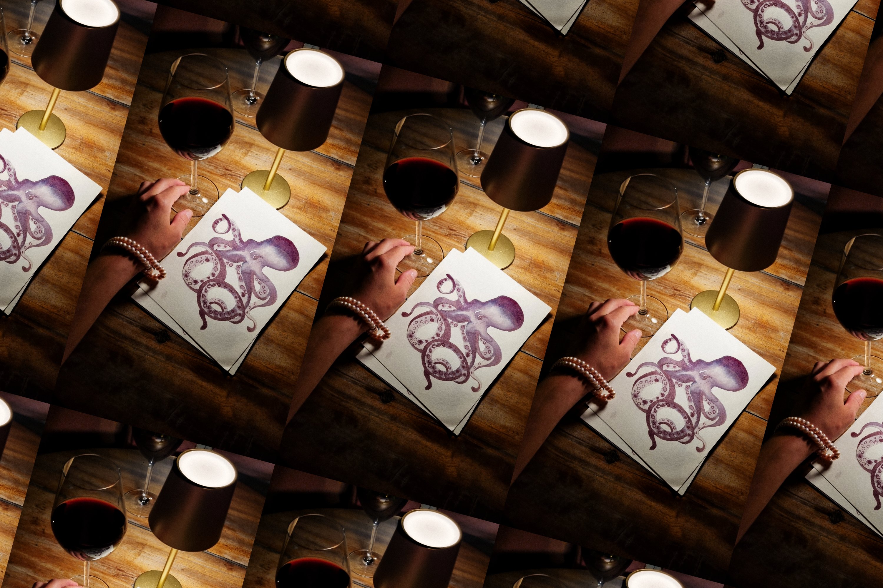 Repeating tiled pattern of a hand-painted purple octopus on paper beside a glass of red wine and a gold table lamp